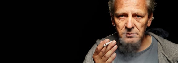 Adult male smoking a cigarette blowing smoke out of his nose.