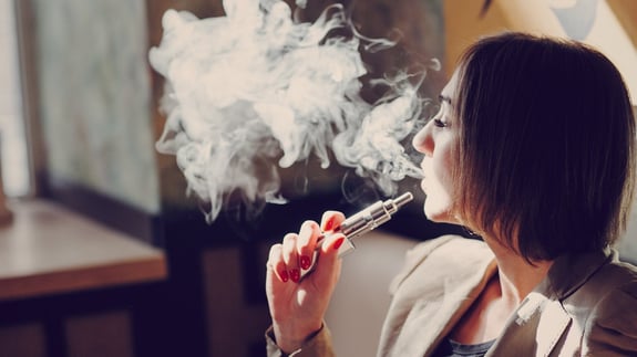 Young adult female using a vaping device blowing aerosol.