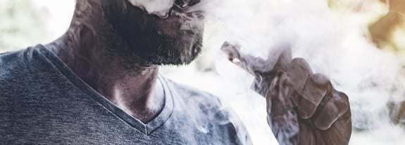 Adult African American male using a vape device and blowing a vape mist.