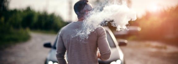 Adult male outside smoking and exhaling a cloud of smoke.