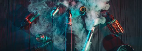 A swirling cloud of vaping mist covering vaping devices and vials of vaping juice.
