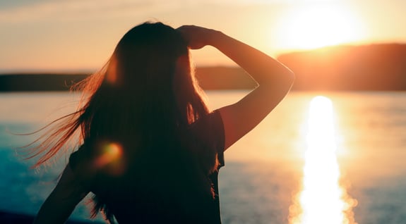 Silhouette of young adult female looking off into the sunset shading her eyes with her hand.