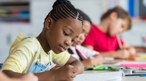 African American female elementary aged student writing in a classroom.