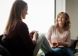 Mom and daughter having a conversation on a window seat. Each holds a mug of hot liquid.