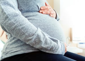 Pregnant woman cradling her abdomen with her hands.
