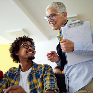 Adult educator looking over a young adult student's shoulder.