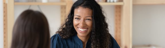 Smiling woman with black curly hair talking with another person