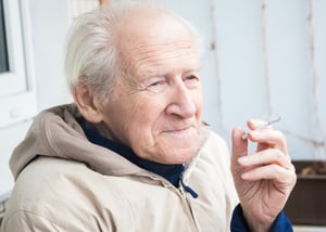 Senior adult male smoking a cigarette outside.