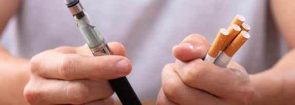 Hands holding cigarettes and a vape device.