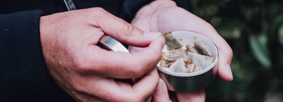 Adult male holding a tin of smokeless tobacco.