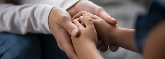 Female parent holding the hands of a younger child.