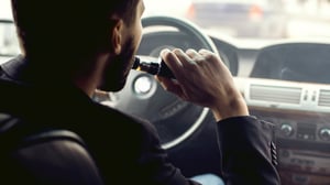 Adult male using a vaping device while driving a car.