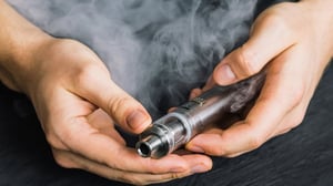 Hands holding a vaping device with vaping mist around.