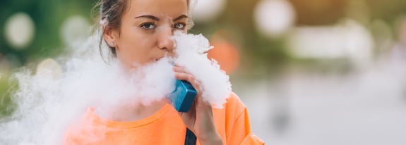 Young adult female using a vaping device and blowing vaping mist.