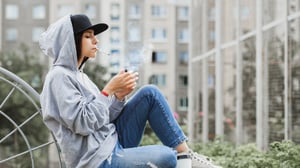Young female adult wearing a hoodie and smoking a cigarette.