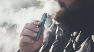 Adult male using a disposable vaping device and blowing a vaping mist.