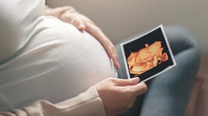 Pregnant woman with a hand on her abdomen looking at an ultrasound image of her baby.
